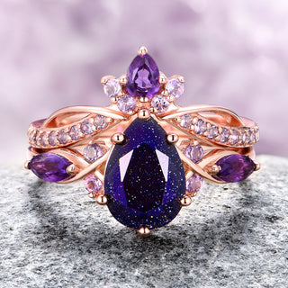An image of a rose gold ring set featuring a large blue center stone with smaller purple accents on a textured background.