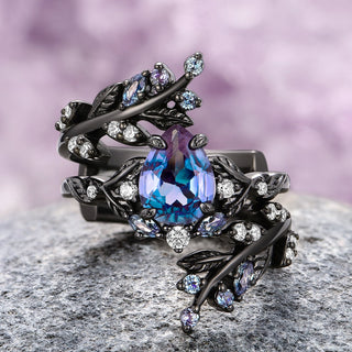 A two-piece sterling silver engagement ring set with a black rhodium finish, featuring a teardrop-shaped lab-grown alexandrite center stone and surrounded by leaf-like designs with smaller simulated diamonds.