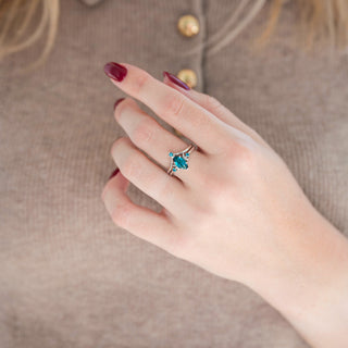 Silver marquise cut teal sapphire engagement ring with crescent moon motif and chevron wedding band held in hand against warm brown background