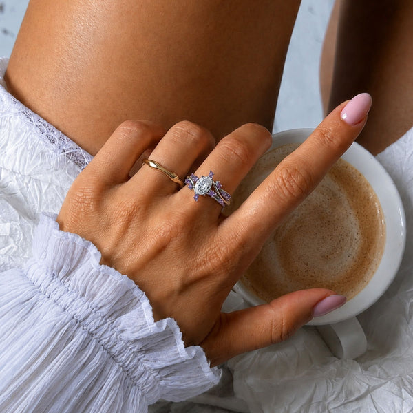 Woman's hand holding a coffee cup while wearing a marquise moissanite and amethyst ring stacked with a plain gold band, Aquamarise lifestyle banner