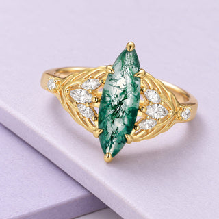 Yellow-gold vermeil leaf ring with a long marquise moss agate and clear accents, photographed on broad pale-lilac tiles.