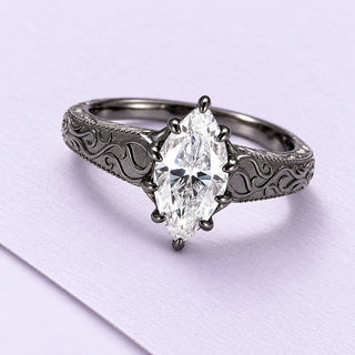 Marquise moissanite ring in dark Victorian filigree metal, angled on a broad lilac paper sheet in soft daylight.