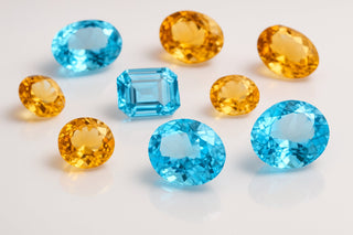 Loose faceted gemstones in sky blue and golden yellow, cut as ovals, rounds and an emerald cut, on a white surface