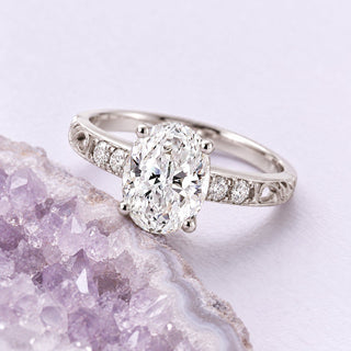 White-gold oval diamond filigree engagement ring resting beside a naturally cropped pale lavender amethyst geode.