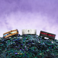 Three handcrafted men's wedding bands with meteorite, moss agate and galaxy inlays on a textured surface with a purple gradient background