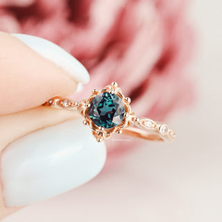 Vintage Alexandrite Fairytale Engagement Ring in 14K Rose Gold Vermeil by Aquamarise, featuring a deep teal color-shifting gemstone and intricate rose gold detailing held by pale nails.