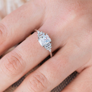 White gold engagement ring with emerald cut diamond center stone and accents on hand over light background