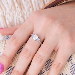 White gold engagement ring with emerald cut diamond center stone and accents on hand over light background