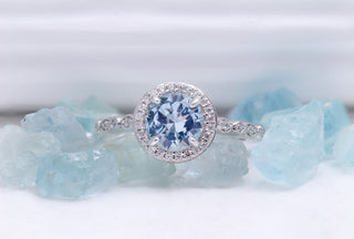 Art Deco Aquamarine Engagement Ring by Aquamarise, shown against pale blue rough aquamarine in an Art Deco halo setting.