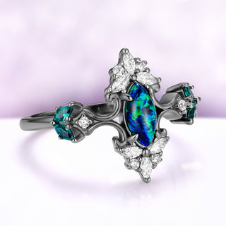 Angled view of the Artemisia peacock fire opal ring, showing the cubic zirconia crown above and below the opal and the simulated teal sapphire cluster on the shoulder