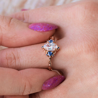 Rose gold engagement ring with oval cut diamond center stone and lab-grown alexandrite accents on hand over a light background 