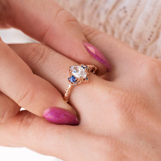 Rose gold engagement ring with oval cut diamond center stone and lab-grown alexandrite accents on hand over a light background 