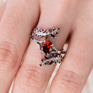 White gold ring set with oval cut natural red garnet center stone and accents on hand over a light background