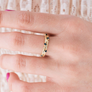 Yellow gold wedding band with black diamond accents on hand over light background