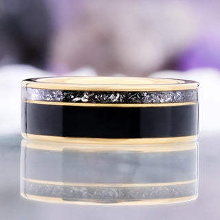 Front view of the yellow gold tungsten band on a reflective surface showing the crushed meteorite texture above the polished black onyx