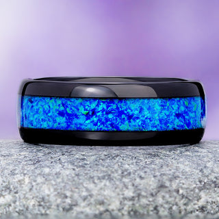 Blue opal black tungsten wedding band on granite, showing the green and violet flash in the crushed opal