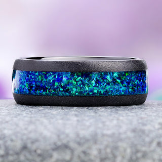 Peacock opal black tungsten wedding band on granite, showing the green, teal and violet flash in the crushed opal