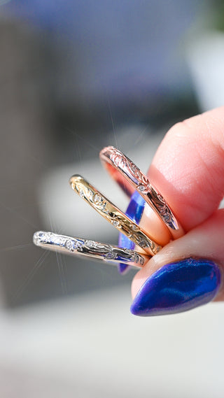 Three gold rings on a finger with blue nail polish against a blurred background