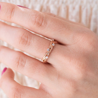 Rose gold wedding band with round diamond accents on hand over light background