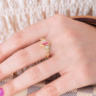 Yellow gold ring with marquise cut pink sapphire center stone and diamond accents on hand over a light background 