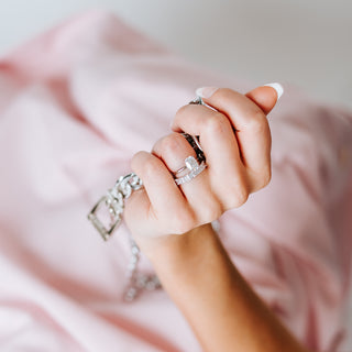 Hand holding a chain with a diamond ring and band on a pink background