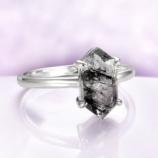 Silver ring with a large, faceted gemstone on a light purple background