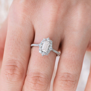 White gold engagement ring set with emerald cut diamond center stone and accents on hand over a light background 