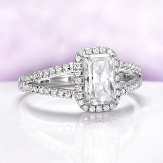 Diamond ring with emerald-cut center stone on a white surface with a light purple background