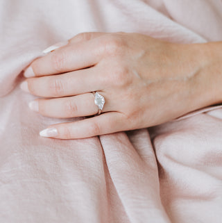 Engagement ring with diamond center stone on a hand against a pink background 