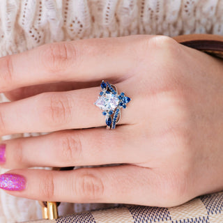 White gold engagement ring set with teardrop cut diamond center stone and lab-grown blue sapphire accents on hand over light background