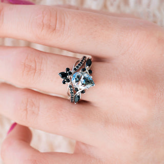 White gold engagement ring set with teardrop gray moissanite center stone and natural black onyx accents on hand over light background