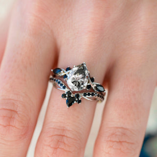 White gold engagement ring set with teardrop gray moissanite center stone and natural black onyx accents on hand over light background