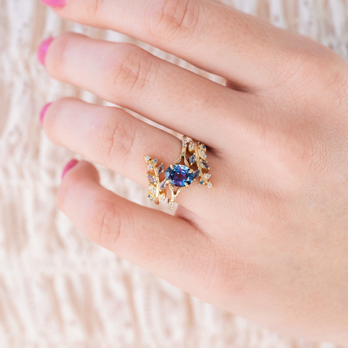 Yellow gold ring with oval cut lab grown alexandrite center stone and diamond accents on hand over a light background