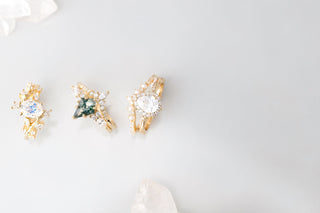 Three gold unique engagement rings with gemstones on a light gray background