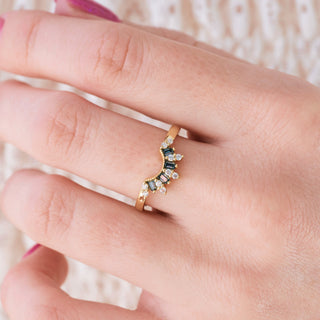 Yellow gold wedding band with crown design and gray moissanite and colorless moissanite accents on hand over light background