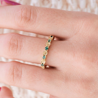 Yellow gold wedding band with rose design and green moss agate accents on hand over a light background 