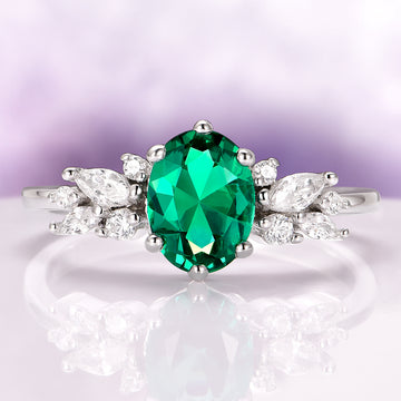 Lily Vintage Emerald Flower Engagement Ring in 14K White Gold by Aquamarise Gold featuring an oval lab-grown emerald with marquise and round diamond accents in a vintage floral design.
