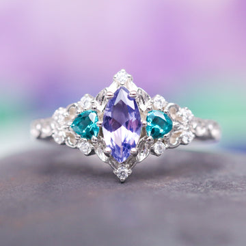 Borealis Tanzanite & Teal Sapphire Couples Ring Set (Mountain Range) by Aquamarise, showcasing a marquise-cut tanzanite flanked by teal sapphire heart accents and delicate diamond details, part of Matching Couples' Rings and September and December Birthstone Jewelry collections.