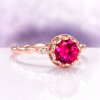 Vintage Ruby Ring in 14K Rose Gold Vermeil by Aquamarise, featuring a vivid red ruby with a delicate twisted band and small diamond accent, styled on a reflective surface with a soft purple background.