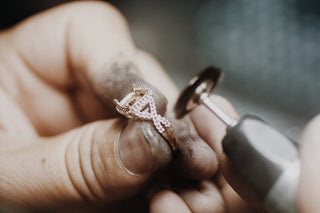 Aquamarise jeweler making the ring. Person holding a rose gold ring with intricate design, using a small tool.