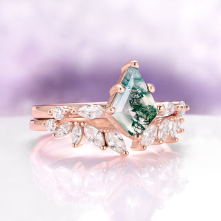 Rose gold ring with green gemstone and clear stones on a reflective surface with a blurred background