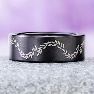 Laurel etched black titanium wedding band on granite, showing the wave of silver-gray leaves around the 8mm flat band