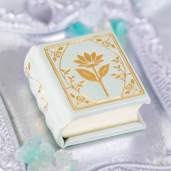 Spring Court Handmade Leather Book Ring Box- Bloomlight Green Edition (Small) by Aquamarise, a delicate white leather ring box with gold floral design on an elegant silver tray.