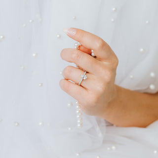 Hand holding a pearl necklace with a diamond ring on a light background