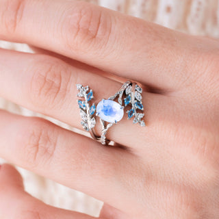 White gold ring set with oval cut natural rainbow moonstone center stone and aquamarine accents on hand over a light background