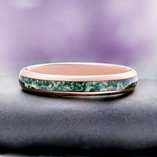 Moss Agate Wedding Band in Rose Gold Tungsten Carbide (4mm) by Aquamarise, resting on a dark stone pedestal to show the green moss agate inlay.