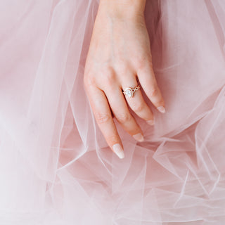 Hand wearing a rose gold diamond ring with pink tulle fabric in the background