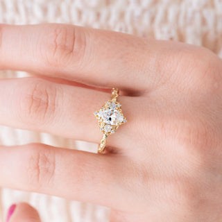 Yellow gold engagement ring with oval cut diamond center stone and diamond accents on hand over a light background 
