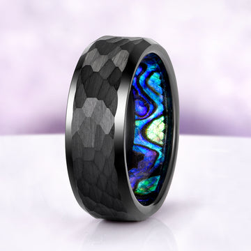 Ring with black textured band and colorful abalone shell inlay on a white background