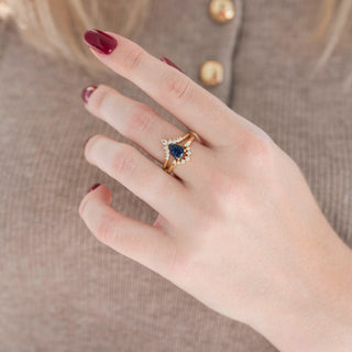 Yellow gold pear/teardrop-cut sparkly blue sandstone engagement ring with diamond accent stones and curved wedding band with diamonds held in hand against warm brown background